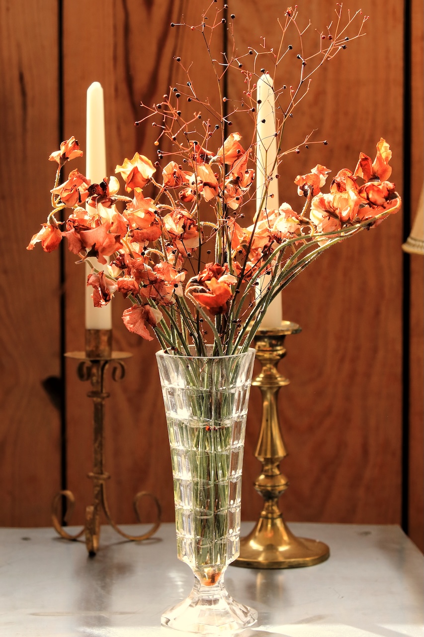 Bouquet de fleurs séchées dans un vase en verre devant deux bougeoirs en laiton