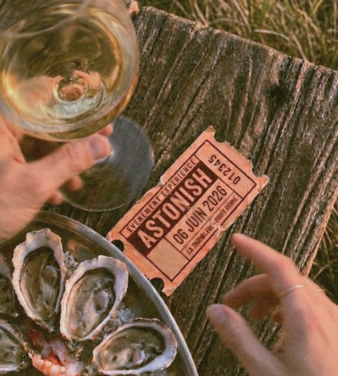 Billets Astonish, huîtres et verre de vin posés sur une planche de bois