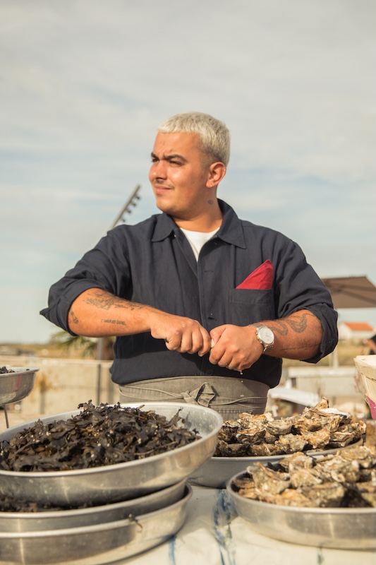 Chef ouvrant des huîtres devant des bacs de fruits de mer
