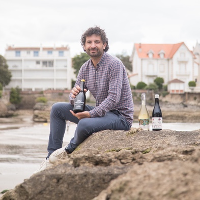 Julien Bonneau, vigneron, assis sur un rocher au bord de l'estuaire avec ses bouteilles