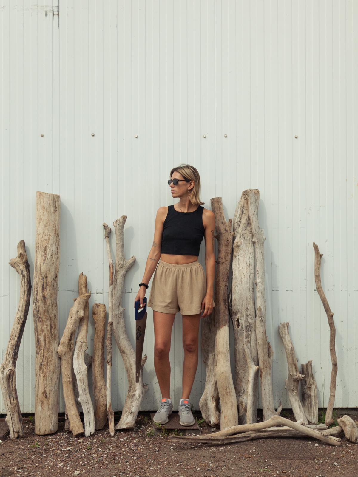 Fleur Bleue, artiste, adossée à une paroi blanche entourée de bois flotté