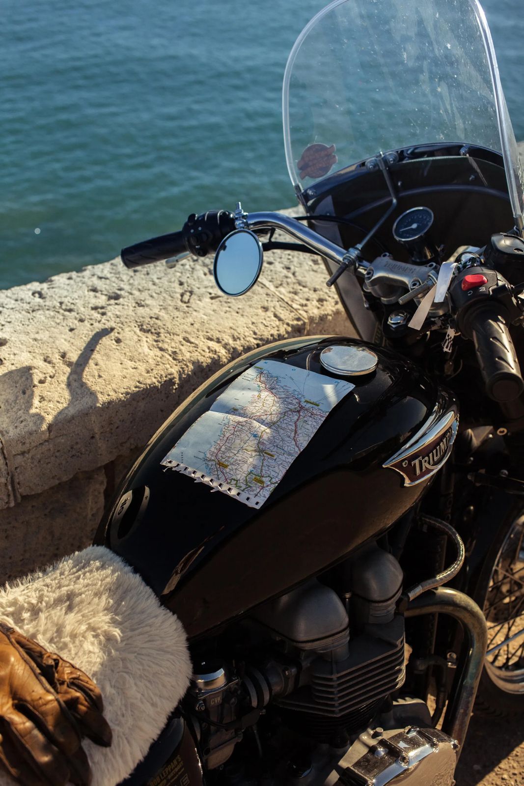 Moto garée face à la mer, carte routière posée sur le réservoir