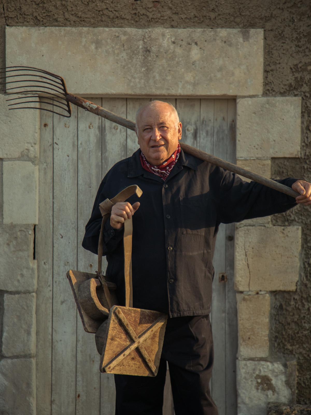 Jacky Leconte, ostreiculteur, portant une fourche et un panier en bois devant une cabane en pierre
