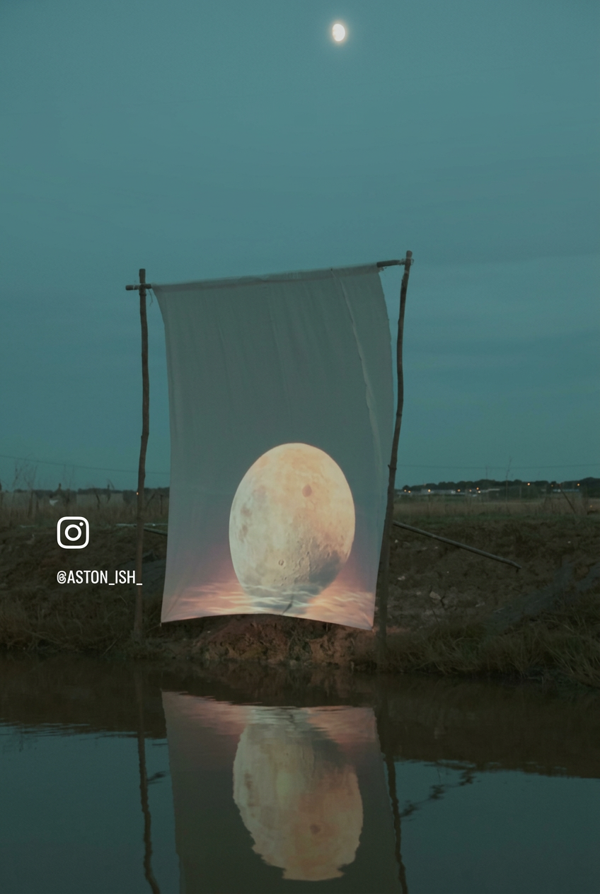 Lune projetée sur une voile blanche tendue au-dessus de l'eau, la nuit, avec son reflet dans la claire